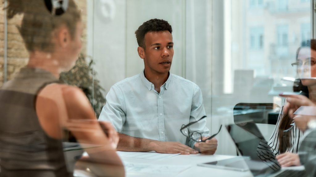 Business expert. Young afro american man holding eyeglasses and explaining something to his