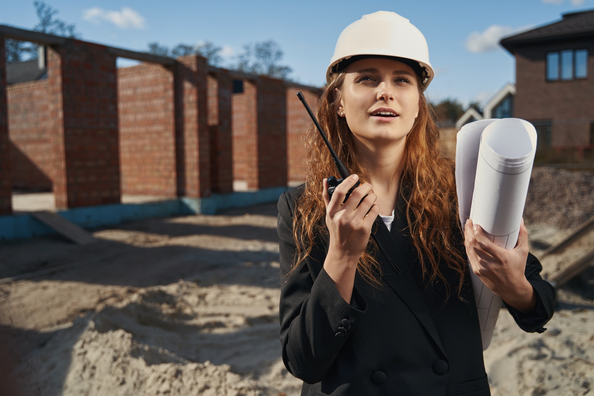 Female engineer with blueprint talking into walkie-talkie